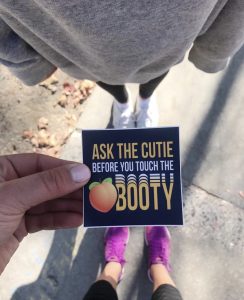 Person holding a sticker that reads, "Ask the cutie before you touch the booty"